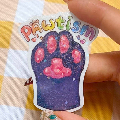 Sticker with paw print and 'PAWtism' text held by a hand on a checkered background